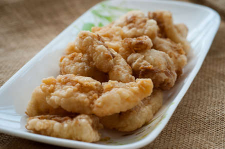 Malaysian style battered and deep fried dory fish cubes. Served in a long plate on a brown background.の写真素材