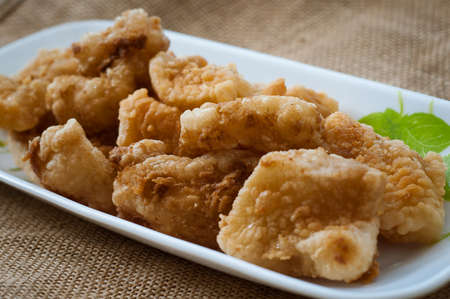 Malaysian style battered and deep fried dory fish cubes. Served in a long plate on a brown background.の写真素材