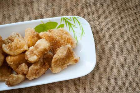 Malaysian style battered and deep fried dory fish cubes. Served in a long plate on a brown background.の写真素材