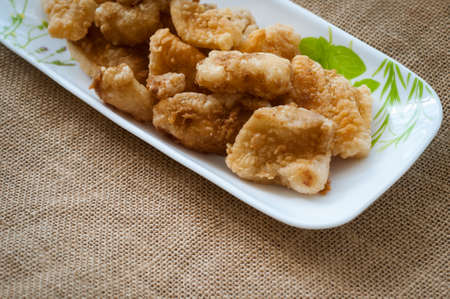 Malaysian style battered and deep fried dory fish cubes. Served in a long plate on a brown background.の写真素材