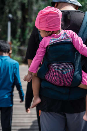 Man with a baby in a sling behind his back walking with the children in a sunny day.の写真素材