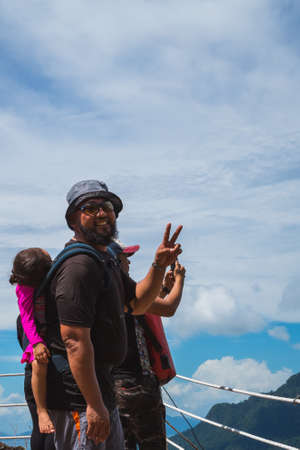 Bearded father with her toddler daughter in ergonomic baby carrier on back outside in mountain nature, show peace sign.の写真素材