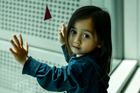 Beautiful portrait of cute little Asian toddler girl. Curious baby child looking away from the window.の写真素材