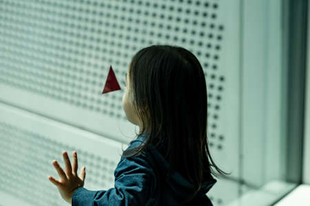 Beautiful portrait of cute little Asian toddler girl. Curious baby child looking at the triangle mark on the window.の写真素材