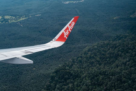 Tawau, Malaysia - Nov 24, 2019: Air Asia aircraft wing flying over green forests and farms on a sunny day.のeditorial素材