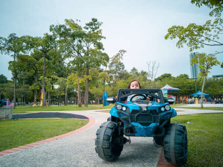 An Asian kid driving electric toy car in a tropical park. Outdoor toys. Children in battery power...