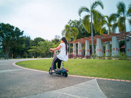 A nice Asian young girl is riding a scooter. Active leisure in the park. Children's sportsの写真素材