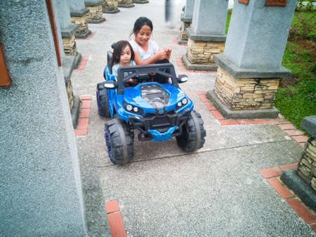 An Asian kid driving electric toy car in a tropical park. Outdoor toys. Children in battery power...