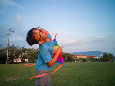 Asian young boy in blue shirt playing with the kite in the field in the parkの写真素材