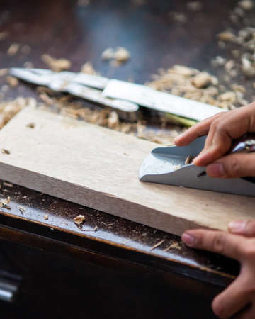 Wood shavings carpenter working with a metal spokeshave and a blurry background. Light beige colored...