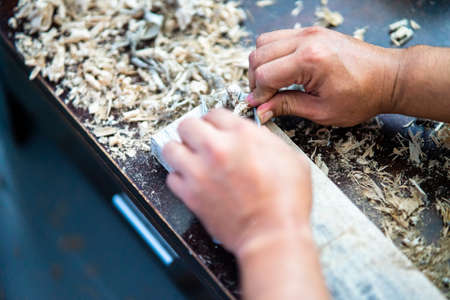 Wood shavings carpenter working with a metal spokeshave and a blurry background. Light beige colored...