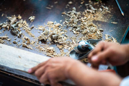 Wood shavings carpenter working with a metal spokeshave and a blurry background. Light beige colored...
