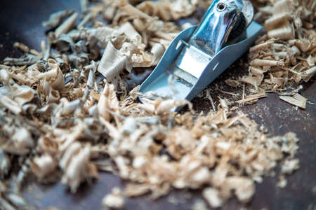 Wood shavings carpenter working with a metal spokeshave and a blurry background. Light beige colored poplar wood with slight curves in it. Vintage woodworking, handwork, handmadeの写真素材
