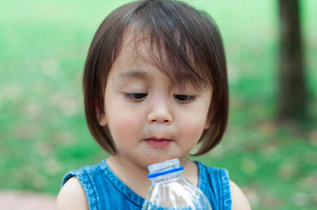 Asian toddler girl drinking water from the plastic water bottle.