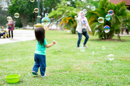 Lovely active little asian girl playing with soap bubble outdoor in the parkの写真素材