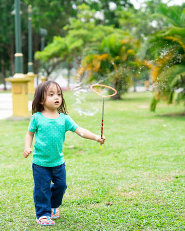 Lovely active little asian girl playing with soap bubble outdoor in the parkの写真素材