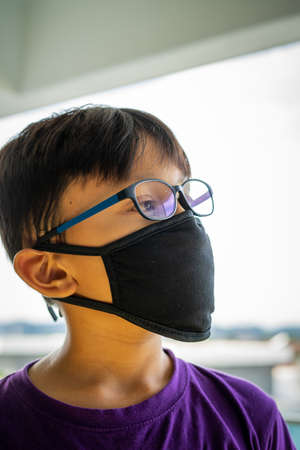 Lockdown and school closures. School boy wearing glasses showing outdoor reflection light with face mask feeling bored and depressed at home. COVID-19 pandemic and Coronavirus Outbreak.の写真素材