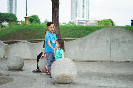 Asian children sitting on the concrete sphere ball shape in the park.の写真素材