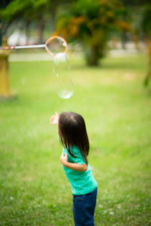 Blurry photo of child playing floating soap bubbles in the garden park.の写真素材