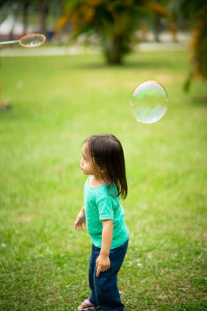 Lovely active little asian girl playing with soap bubble outdoor in the park