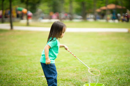 Lovely active little asian girl playing with soap bubble outdoor in the parkの写真素材