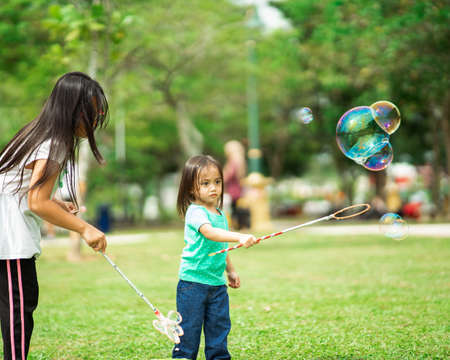 Lovely active asian girl siblings playing with soap bubble outdoor in the park