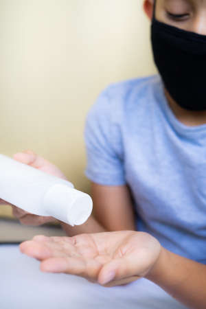 Young boy wearing mask is holding alcohol antiseptic gel bottle to clean hands and prevent germs.の写真素材
