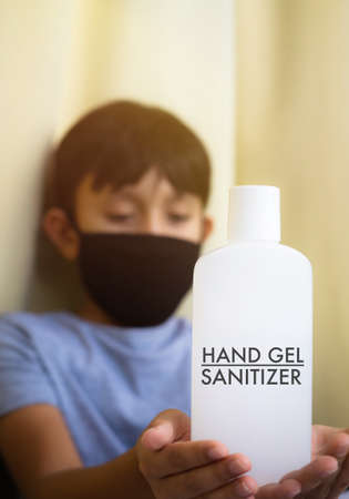 Young boy wearing mask is holding alcohol antiseptic gel bottle to clean hands and prevent germs.の写真素材