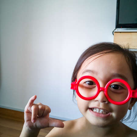Happy toddler girl playing with red fake sunglasses at home.の写真素材