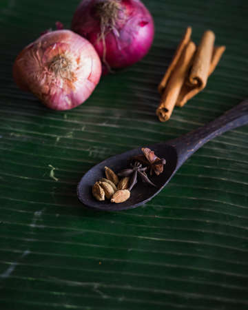 Cooking spices on banana leaf. Cardamom, star anise, cinnamon and onions. Buah pelaga, bunga lawang, kayu manis and bawang besar.の写真素材