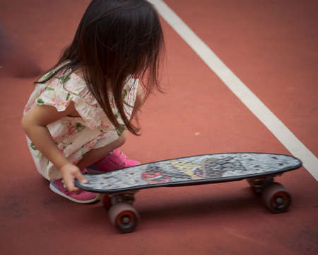 Toddler girl moving a penny board, skateboard at the basketball court. motion shot.