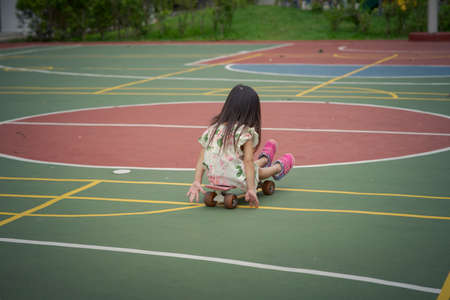 Toddler girl sitting on a penny board, skateboard at the basketball court.の写真素材