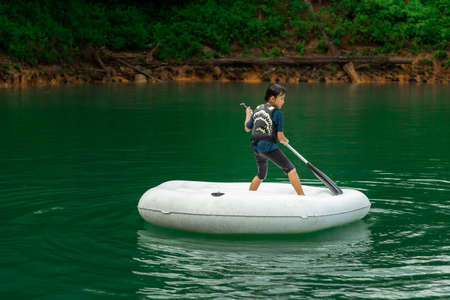 Asian boy wearing life jackets paddling on an inflatable boat in Kenyir Lake, Malaysia.