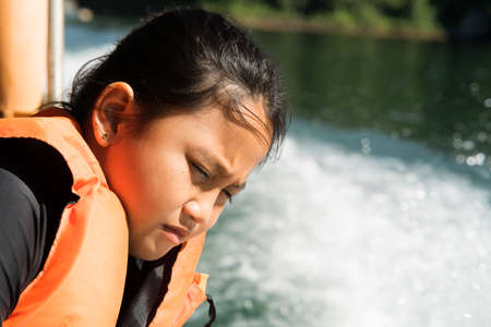 Casual portrait of little girl wearing life jackets in outdoor on summer day enjoying boat ride or fishing tripの写真素材