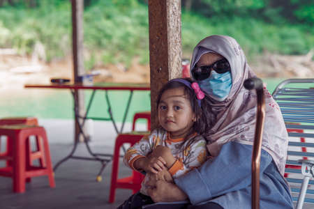 Grandmother in hijab wearing face mask hugging toddler grand child in outdoor.の写真素材