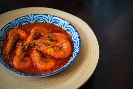 "Sambal Udang" or Spicy Chili prawns in a blue and wooden plate over wooden background. South East Asian cuisine food.の写真素材