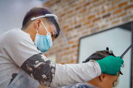 Children hairdresser with scissors is cutting little boy against in a barber shop.