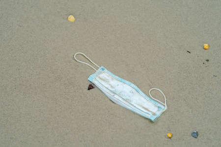 Coronavirus covid-19 pollution disease the environment. Used surgical mask thrown on the seashore of a beach.の写真素材