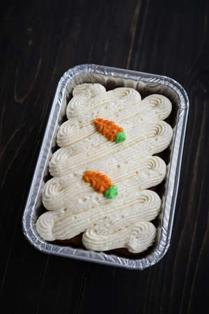 Carrot cake and cream cheese in an aluminium container. Wooden background.