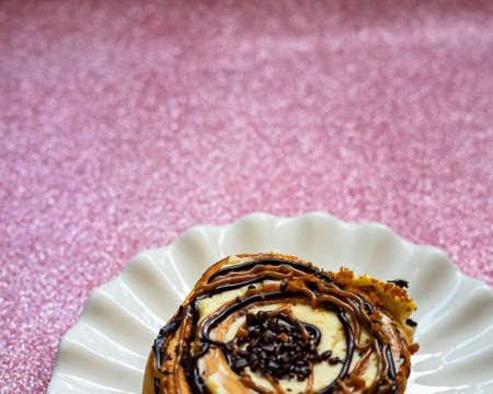 Cinnamon rolls with various sweet toppings and chocolate on a white plate on the pink glitter...