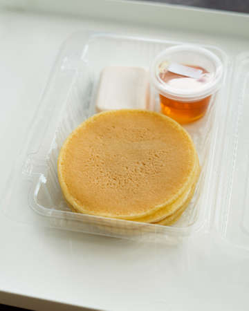 Stack of pancakes in a container transparent clear box with honey and butter isolated on white background.の写真素材