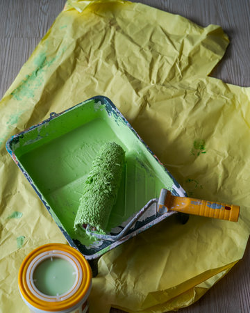 Paint roller in paint tray with green color in the tray on yellow paper.