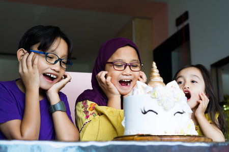 Three Asian siblings celebrating birthday at home. Looking at the cake with jaw dropping.の写真素材