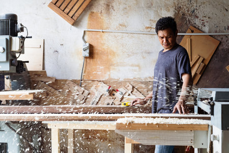 Negeri Sembilan, Malaysia - Dec 12, 2020:  Carpenter at work sanding the wood with sanding machine blurry background. Mature man with carpenting tools.のeditorial素材