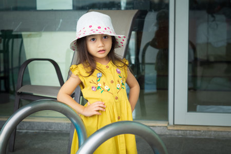 Portrait of beautiful little gorgeus lovely toddler girl in mustard summer look clothes, fashion dress, and hat. Happy healthy asian child posing in outdoor.の写真素材