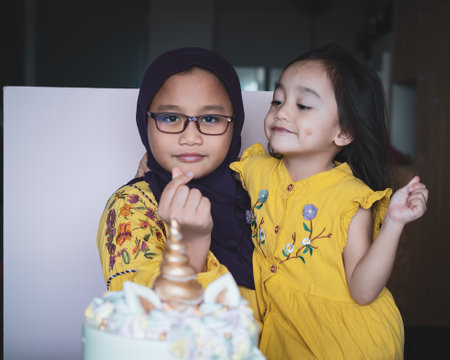 Portrait of a young girl wearing glasses and hijab smiling and showing love sign while carrying little sister in her arm.の写真素材