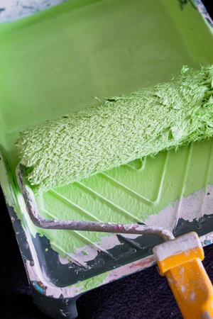 yellow holder attached to the roller in a tray with green paint color on yellow paper.の写真素材