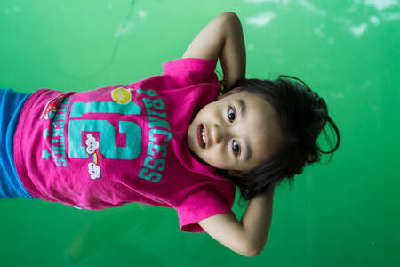 Portrait of a little girl lying on the clear transparent glass against the sea water.の写真素材