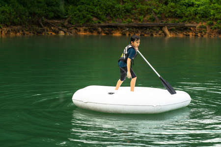 Boy wearing life jackets paddling on an inflatable boat in a lake.の写真素材