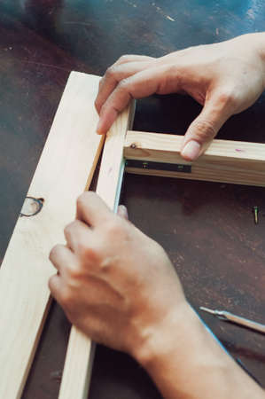 Woodworking with a drill to screw angle bracket in a wooden block with wood shavings and smoke in a...